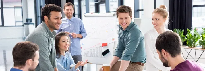 Group of people gathered around a whiteboard with charts and notes in an office setting.